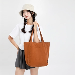 Détail du sac fourre-tout marron caramel montrant le tissu durable et la poche avant