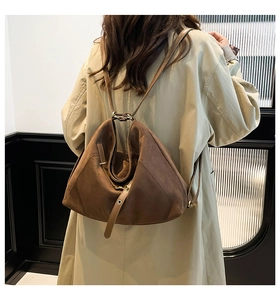 Brown suede backpack with geometric folding design and gold rings worn with beige coat