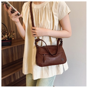 Close-up of brown vintage crossbody bag with a circular metal logo on textured leather
