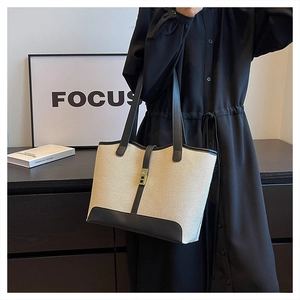 Detail of beige canvas tote bag with black leather straps and metal buckle closure