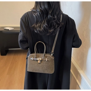 Détail d'un sac coquille en daim gris avec fermoir métallique et bandoulière réglable