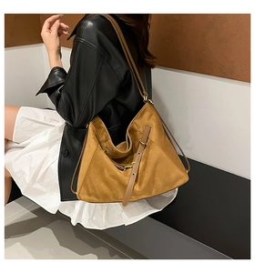 Detail of a large suede hobo bag in mustard yellow featuring a slim shoulder strap and buckle