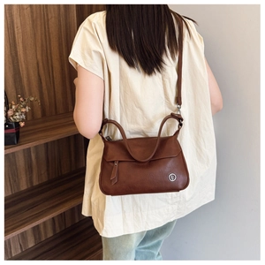 Detail shot of vintage dark brown faux leather bag with round metal logo and leather puller