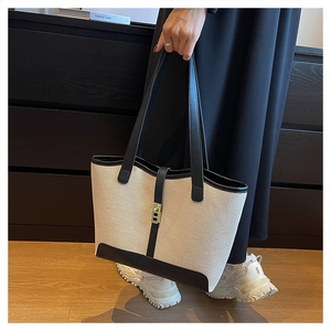 Detail of canvas tote bag featuring black leather trim and golden metal swivel lock