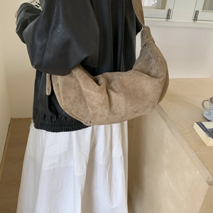 Side view of a large camel suede croissant bag worn over the shoulder in a cozy room