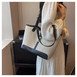Detailed view of large tote bag featuring beige canvas and black leather strap patchwork