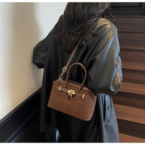 Détail d'un sac en daim marron avec fermoir doré porté par un mannequin en veste de cuir noir