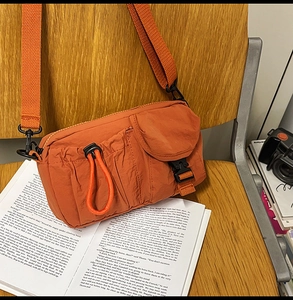 Detail of orange nylon crossbody bag featuring front drawstring pocket and adjustable strap
