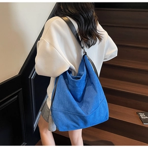 Detail of blue suede oversized tote bag with black leather strap on a model's shoulder