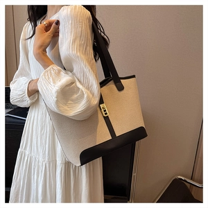 Detailed view of beige canvas tote bag with black leather trim and gold metal clasp
