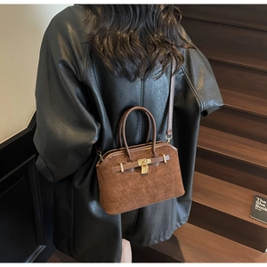 Gros plan du sac coquille en daim marron avec boucle dorée et lanières en cuir