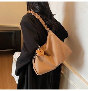 Détail d'un grand sac cabas en cuir marron avec bandoulière plissée et peluche ours
