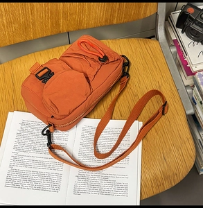 Detail of orange quilted nylon crossbody bag with detachable mini pouch and utility buckle
