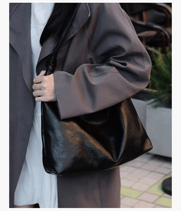 Side view of large black tote bag with wrinkled texture on woman in grey trench coat
