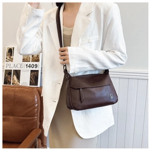 Detail of vintage dark brown leather shoulder bag with silver logo on white blazer model