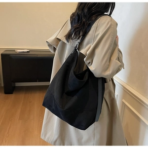 Detailed view of a black minimalist oversized tote bag worn by a model in a cozy interior