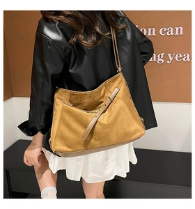 Detail of a large ginger suede tote bag worn on shoulder by model in a minimal room