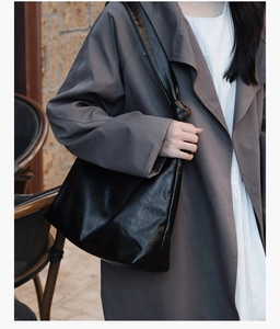 Close-up of a large black leather tote bag featuring glossy texture and wide shoulder strap