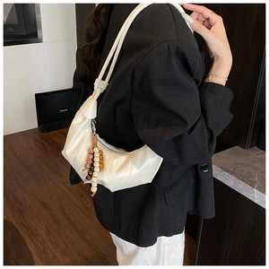Close-up of cream PU leather dumpling bag with decorative wooden beaded tassel detail