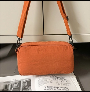 Detailed view of burnt orange nylon crossbody bag with adjustable wide fabric strap