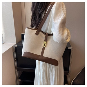 Detail of canvas tote bag with brown leather trim and golden twist lock on shoulder