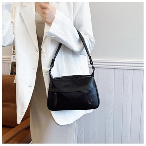 Detail showing high-quality black leather texture and circular metal logo on shoulder bag