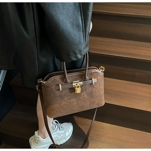 Détail d'un sac coquille en daim marron avec boucle dorée et doubles poignées femme