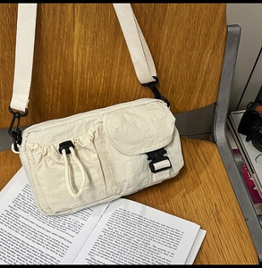 Detail of off-white nylon utility bag with drawstring pocket and black buckle strap