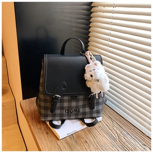 Detail of a mini backpack with grey plaid pattern and a white plush dog keychain