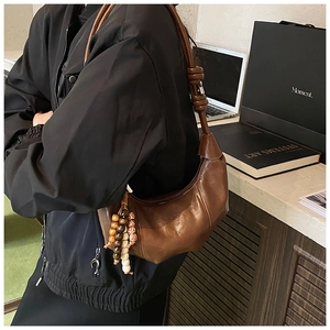 Detail of a brown leather dumpling bag featuring unique pleats and bohemian beaded charms