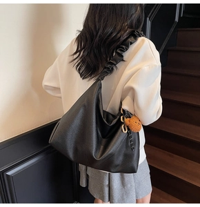 Gros plan d'un grand sac cabas noir en cuir litchi avec bandoulière plissée et ourson