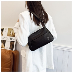 Detail of a black minimalist underarm bag with a smooth leather finish and metal logo