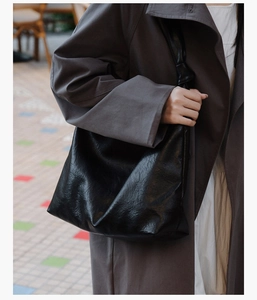 Detail of a black large-capacity leather tote bag with wide strap worn by a model