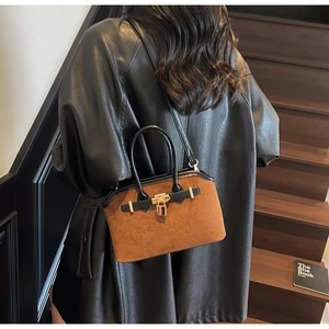 Détail d'un sac shell en daim marron avec lanières en cuir noir et fermoir métallique