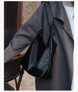Detail of black glossy leather tote bag featuring a decorative knotted shoulder strap detail