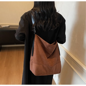 Close-up of a large brown suede tote bag featuring black leather straps and stitch details