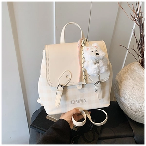 Detail of cream backpack with checkered pattern, buckle closure, and plush dog charm