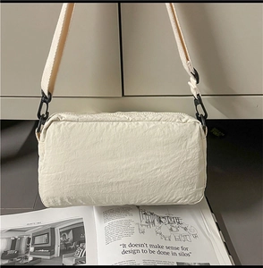 Detail of off-white nylon crossbody bag with wide strap and black buckles on magazine