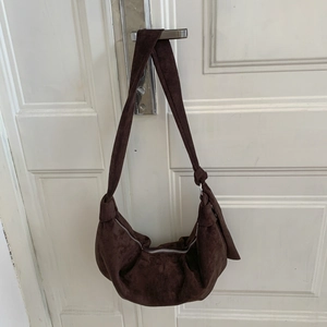 Detail of dark brown suede hobo bag with knotted strap and silver zipper closure