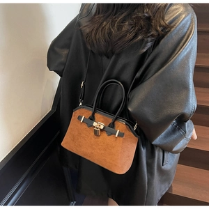 Vue latérale d'un sac shell en daim caramel porté avec un manteau en cuir noir