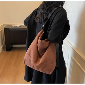 Brown matte suede Hobo tote bag with black wide strap worn by a model in a minimalist room
