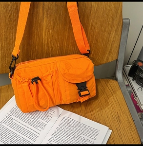 Detail of vibrant orange nylon crossbody bag with multi-pocket design on a wooden chair