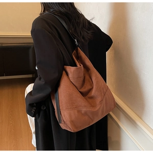 Detail view of large caramel suede tote bag featuring a black wide strap and soft texture