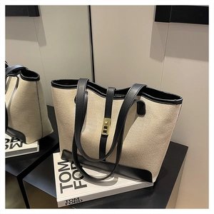 Detail of canvas tote bag with black leather trim and gold metal clasp on a white book