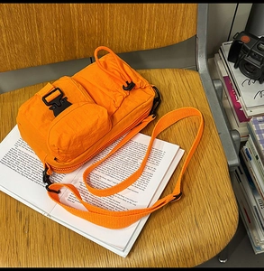 Detail of orange nylon crossbody bag with tactical buckles on a wooden vintage setup