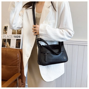 Detail of black pebbled leather shoulder bag with round metal logo worn by a model
