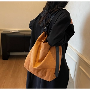 Detail showing high-capacity brown suede tote bag with a black wide shoulder strap on model