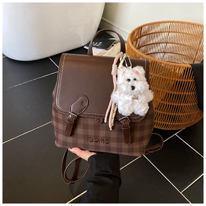 Detail of vintage brown backpack with checkered pattern base and plush dog charm accessory