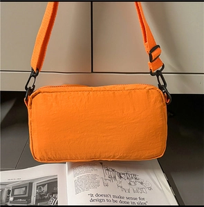 Detail view of orange crossbody bag with crinkled texture fabric and black metal buckle