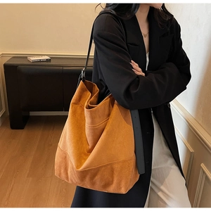 Detail of large orange-brown suede tote bag worn by model in a stylish indoor setting